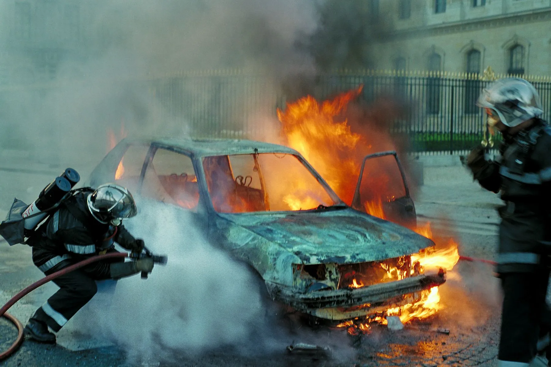 Firefighters spray water on a burning car on a city street