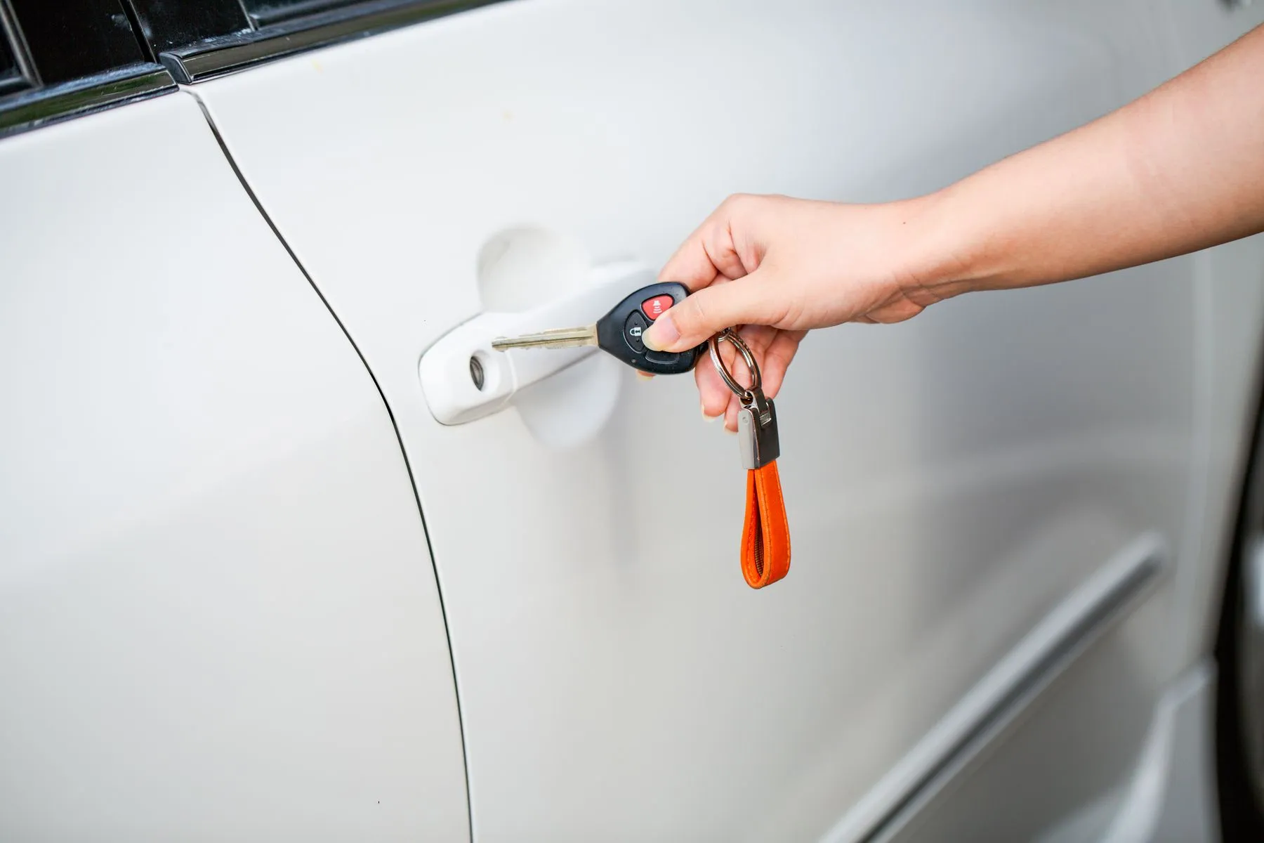 A hand holding a car key with an orange key tag next to a white car door