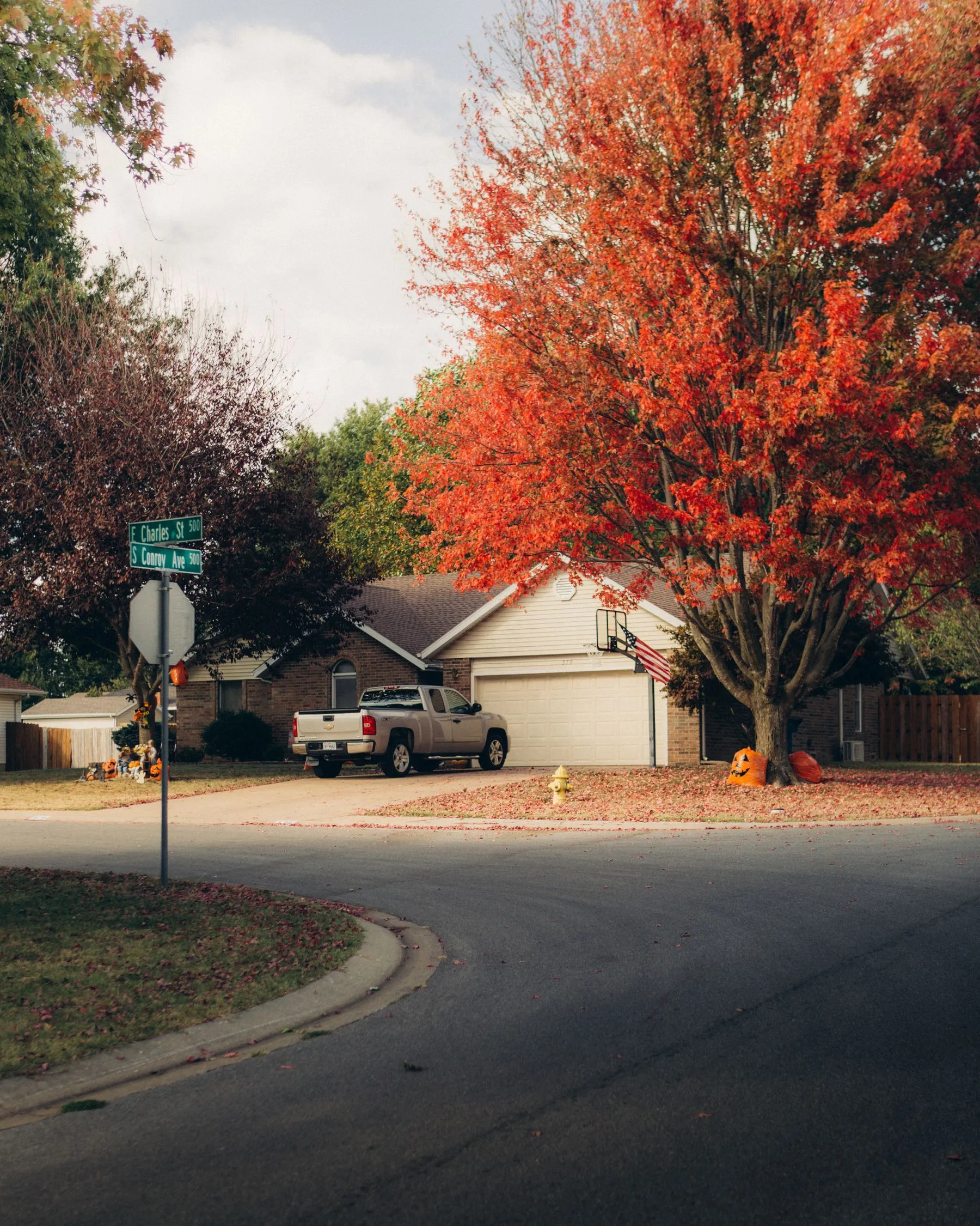 A residential corner with autumn trees and a pickup truck parked in a driveway